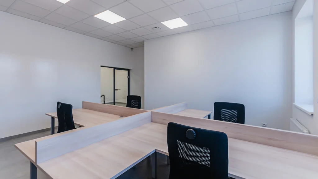An image of a small, contemporary office with empty white walls and empty work stations in the foreground.